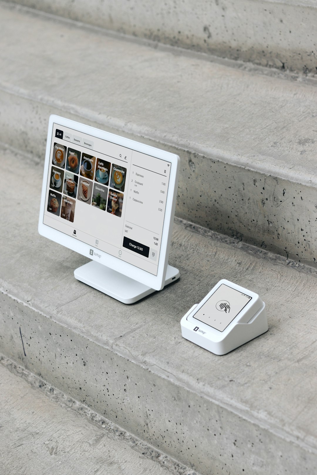 Une installation de point de vente (POS) est présentée sur des marches en béton, avec un écran d’affichage blanc au design moderne, accompagné d’un lecteur de carte compact. L’écran affiche un menu numérique proposant divers produits, tandis que le lecteur de carte est prêt pour les paiements sans contact. Cet ensemble épuré et minimaliste met en avant la portabilité et le design élégant des solutions de paiement SumUp, idéales pour les petites entreprises, les cafés et les commerces de détail qui recherchent à la fois la fonctionnalité et l’esthétique.